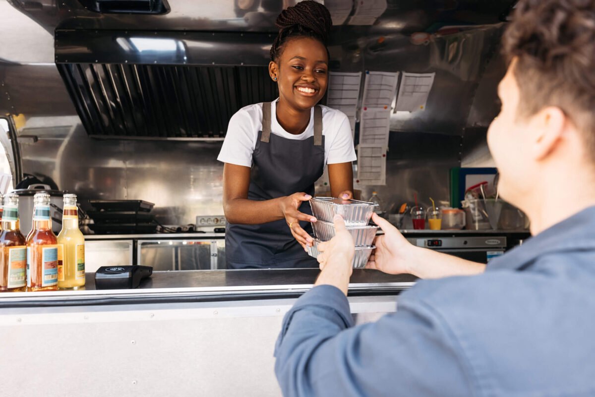 Smiling salesman giving packages with street food to a female customer. Food truck owner serves the buyer.